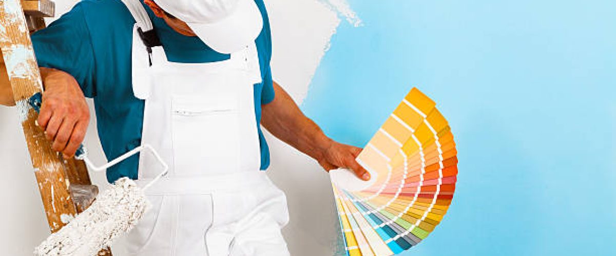 portrait of painter man with paintroller and wooden vintage ladder showing a color palette, on half painted wall